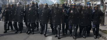 photo d'un front de policiers lourdement armés et protégés avançant vers le photographe
