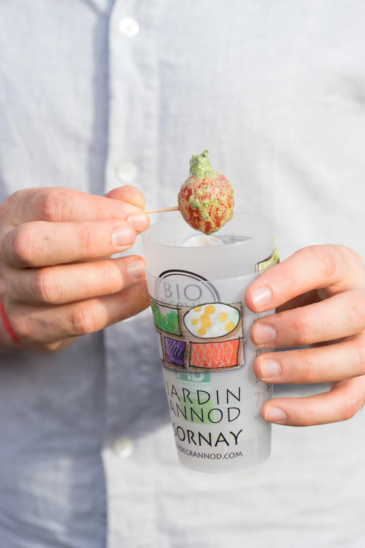 photo d'une main tenant piquée une tomate cerise plongée dans un verre de pesto chèvre basilic