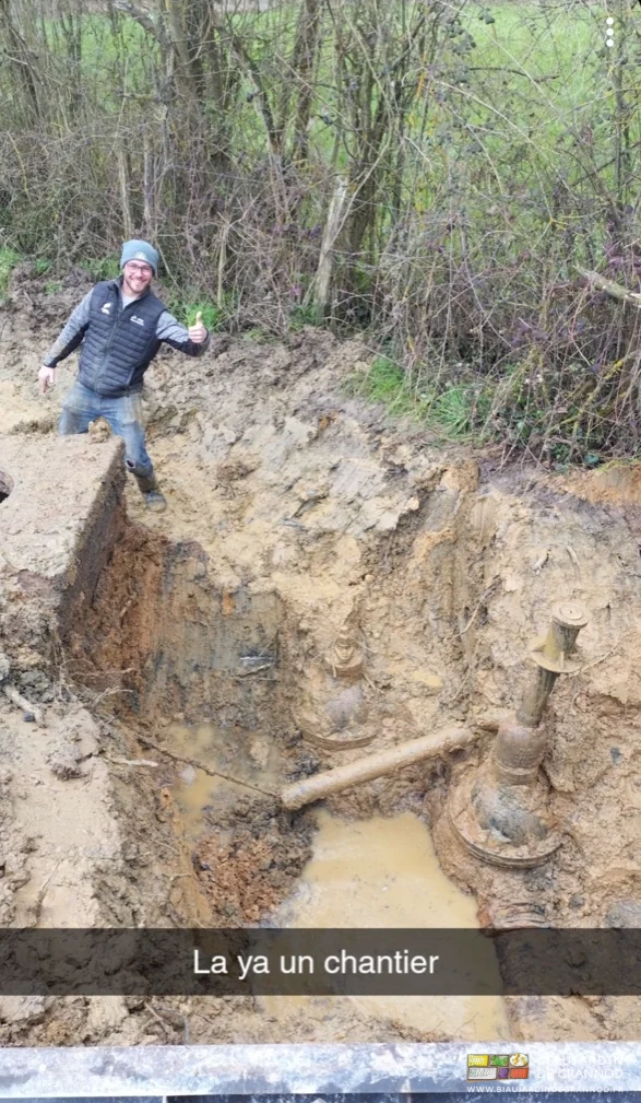 photo de Matthieu souriant au fond d'une tranchée boueuse pour réparer la canalisation